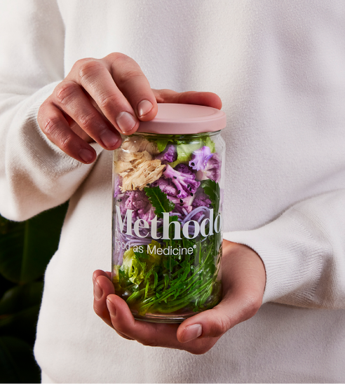 Hand holding a glass jar filled with vegetables